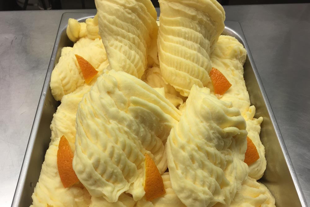 En gelatoglass med apelsinsmak, fint upplagd i en metallbehållare