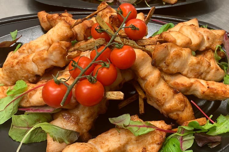 Cateringfat med grillade kycklingspett och färska tomater, vackert upplagda för servering
